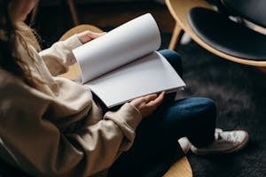 Person in Blue Denim Jeans Holding White Book