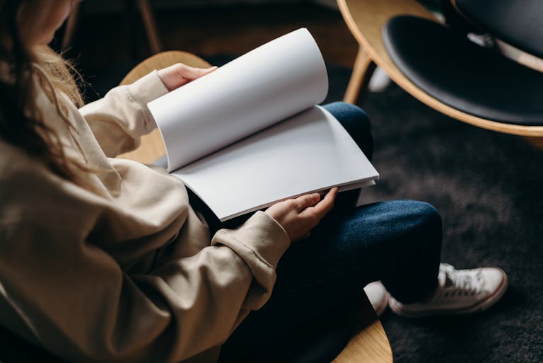 Person in Blue Denim Jeans Holding White Book